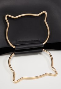 Objet en cuir noir avec poignée en métal doré en forme de chat, montrant le devant et le dos de la poignée sur une surface blanche.