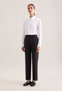 White button-up shirt with long sleeves, paired with high-waisted black trousers. Black loafers complete the outfit. Simple and tailored design.