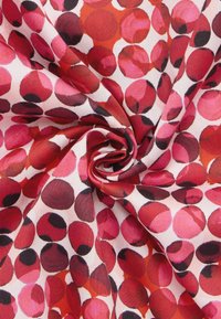 Baumwollstoff mit einem wirbelnden Muster aus roten, rosa und schwarzen Kreisen auf einem weißen Hintergrund, der eine glatte, leichte Textur zeigt.