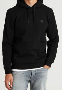 Felpa con cappuccio nera in misto cotone, con cappuccio regolabile con coulisse, polsini e orlo a costine, e una piccola etichetta con il logo sul petto. Abbinata a jeans chiari.