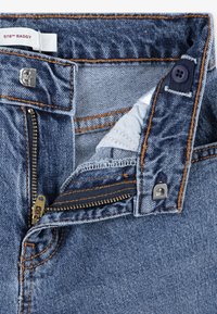 Modré riflové nohavice s voľným strihom. Majú predný zips, zapínanie na gombík a kontrastné oranžové prešívanie pri švoch.