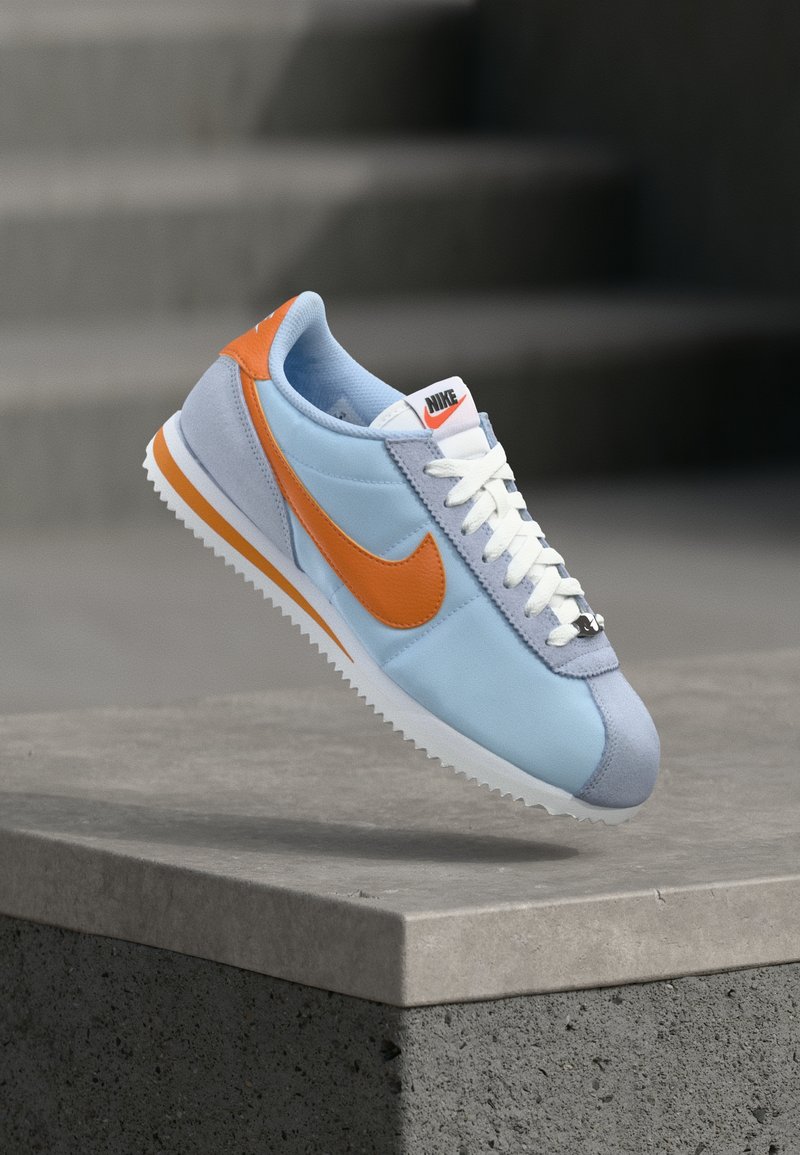 Svijetloplavi Nike tenisice s narančastim naglascima, bijelim vezicama i sivim nubukom na peti. Imaju gumeni potplat i izvezeni logo na jeziku.