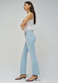 Vaqueros acampanados de color azul claro con una cintura alta, que presentan un diseño clásico de cinco bolsillos y detalles de costura sutiles, combinados con sandalias negras de tacón.