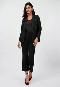 Blazer preto e calças combinando em um tecido suave. O blazer tem lapela e frente aberta, com calças largas até aos tornozelos. Sapatos de salto preto.