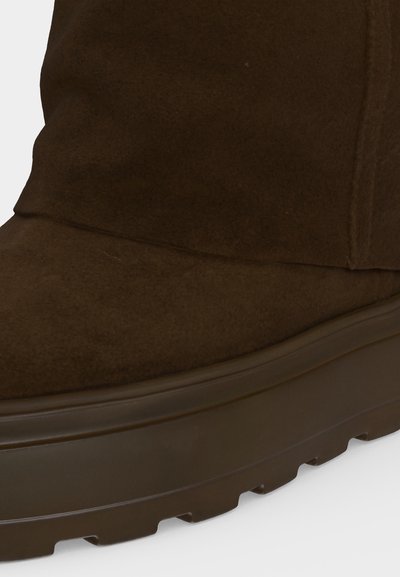 Gros plan d'une botte en daim marron avec une semelle en caoutchouc épaisse et un motif de bande de roulement profond sous la chaussure.