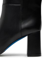 Stivaletto in pelle nera con tacco a blocco quadrato e accento blu sulla suola. Presenta una texture liscia e cuciture pulite lungo le cuciture.