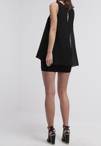 Top nero senza maniche con un design fluido, caratterizzato da una schiena a apertura a chiave e tessuto a strati. Abbinato a una mini gonna nera aderente e sandali con tacco.