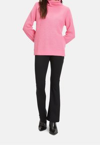 Rosa geripptes Rollkragensweatshirt, kombiniert mit schwarzen ausgestellten Hosen. Das Sweatshirt hat einen lockeren Schnitt und umgeschlagene Bündchen; die Hosen haben eine glatte Textur.