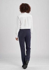 Weißes Hemd mit Kragen und Rückenfalte, kombiniert mit einer dunkelblauen Hose mit elastischem Bund. Aus glattem Stoff und im knöchellangen Design.