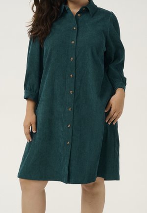 Groenblauw corduroy overhemdjurk met een kraag, driekwart mouwen, knopen aan de voorkant en een losse pasvorm. Soepele textuur en subtiele glans.