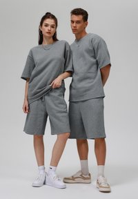 Šedé tričká s bavlnenou zmesou v oversize štýle a šortky s uvoľneným strihom a jemnou textúrou, doplnené o biele a béžové tenisky.