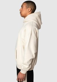 Cremfarbener Hoodie mit einer großzügigen Kapuze, gerippten Bündchen, Seitentaschen und einer lässigen Passform. Hergestellt aus weichem Baumwollmischgewebe.