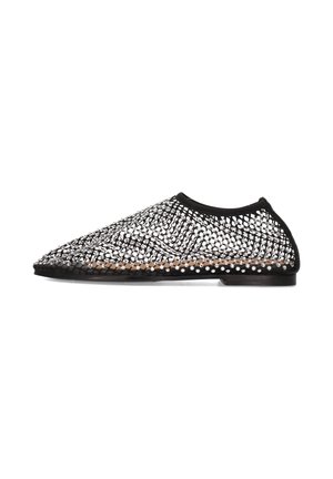 Chaussure en maille noire avec des accents argentés, un bout pointu et une semelle plate. Le design comprend un motif tissé et une tige flexible.