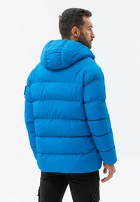 Modrá péřová bunda s kapucí, s prošívaným designem, elastickými manžetami a hladkou texturou. Zadní pohled ukazuje elegantní siluetu.