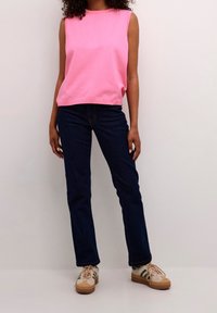 Bezrękawnik w różowym kolorze z okrągłym dekoltem, w zestawie z ciemnoniebieskimi dżinsami. Obuwie charakteryzuje się połączeniem akcentów w kolorze kremowym, brązowym i zielonym.