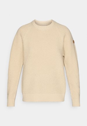 Crème-kleurige gebreide trui met een gestructureerd patroon, ronde hals, en geribde manchetten en onderrand. Heeft een klein rond logo op de linker mouw.