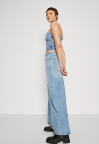 Ensemble en denim composé d'un haut ajusté sans manches et de pantalons larges à taille haute en bleu clair délavé, associés à des bottes à talons blocs noires.