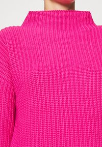 Maglione fucsia a maglia con colletto alto, caratterizzato da una trama a costine e un tessuto spesso e morbido. Adatto per l'abbigliamento casual in climi freschi.