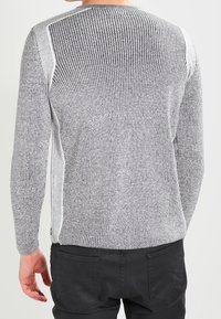 Pull gris clair en maille avec texture côtelée, présentant des panneaux latéraux blancs contrastants, des manches longues et un col arrondi.