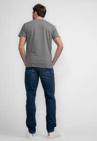 Camiseta de algodón gris con mangas cortas y escote redondo, combinada con jeans azul oscuro y zapatillas blancas, vista desde la parte de atrás.