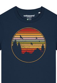 Marineblaues T-Shirt mit einem kreisförmigen Grafikdesign in gestreiften Sonnenuntergangsfarben (rot, orange, gelb) mit Silhouetten von Bäumen und Vögeln.
