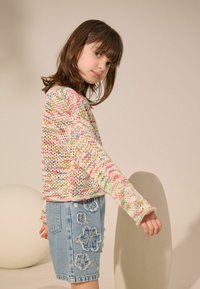 Pull en tricot coloré avec un mélange de teintes pastel, associé à une jupe en denim clair ornée de broderies florales.
