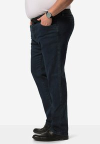 Pantalones vaqueros de mezclilla azul oscuro con corte recto, con trabillas para el cinturón y bolsillos, combinados con zapatos de cuero negros y un reloj de pulsera.