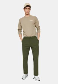 Felpa beige con maniche raglan, pantaloni verde oliva e sneakers bianche con dettagli neri. Design semplice e moderno con una vestibilità dritta.