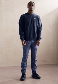 Sweatshirt navy avec des poignets et un ourlet côtelés, associé à un jogging bleu clair à coupe fuselée. Des chaussures de sport noires complètent la tenue.