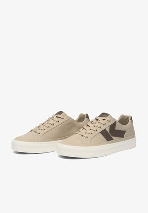 Coppia di sneaker beige basse con suole bianche e accenti marroni a chevron sui lati, con lacci e etichetta brandizzata sulla linguetta.