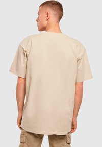 Beige oversized t-skjorte med rund hals og korte ermer, laget av glatt bomullsmateriale, med en enkel bakside og avslappet passform.