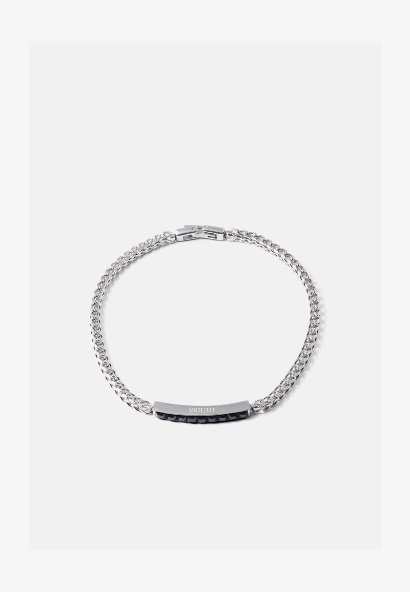 Bracciale in argento con una barra rettangolare incisa con "GUESS" e borchie nere a piramide su uno sfondo bianco.