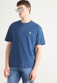Blå bomulds t-shirt med et lille trekantet logo på brystet. Klassisk pasform med korte ærmer og design med rund hals.