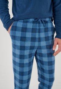 Blauwe geruite fleece pyjamabroek met een elastische tailleband en trekkoord. Kenmerkt afwisselende tinten van licht en donkerblauwe vierkanten.