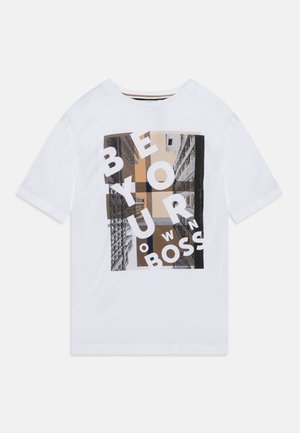 Witte T-shirt met korte mouwen met een grafisch ontwerp van wolkenkrabbers en overlappende witte letters die abstracte tekst vormen in beige en zwarte tonen.