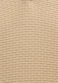 Μπεζ πλεκτό ύφασμα με επαναλαμβανόμενο υφασμάτινο μοτίβο που μοιάζει με αλληλοδεμένα οριζόντια και κάθετα παραλληλόγραμμα.
