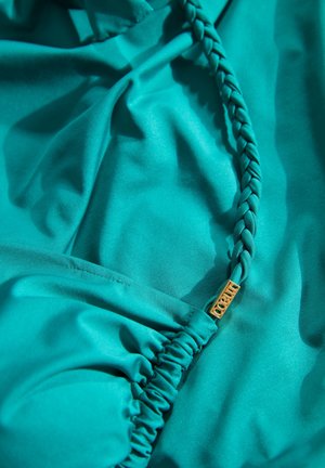 Turkizna tkanina z gladko teksturo, z pletenimi detajli in zlatim okrasjem, zbrane na robovih za dinamičen videz.