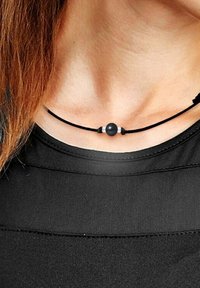 Collier en cordon noir avec une perle noire centrale, accentuée par des détails en argent de chaque côté, porté sur une chemise noire.