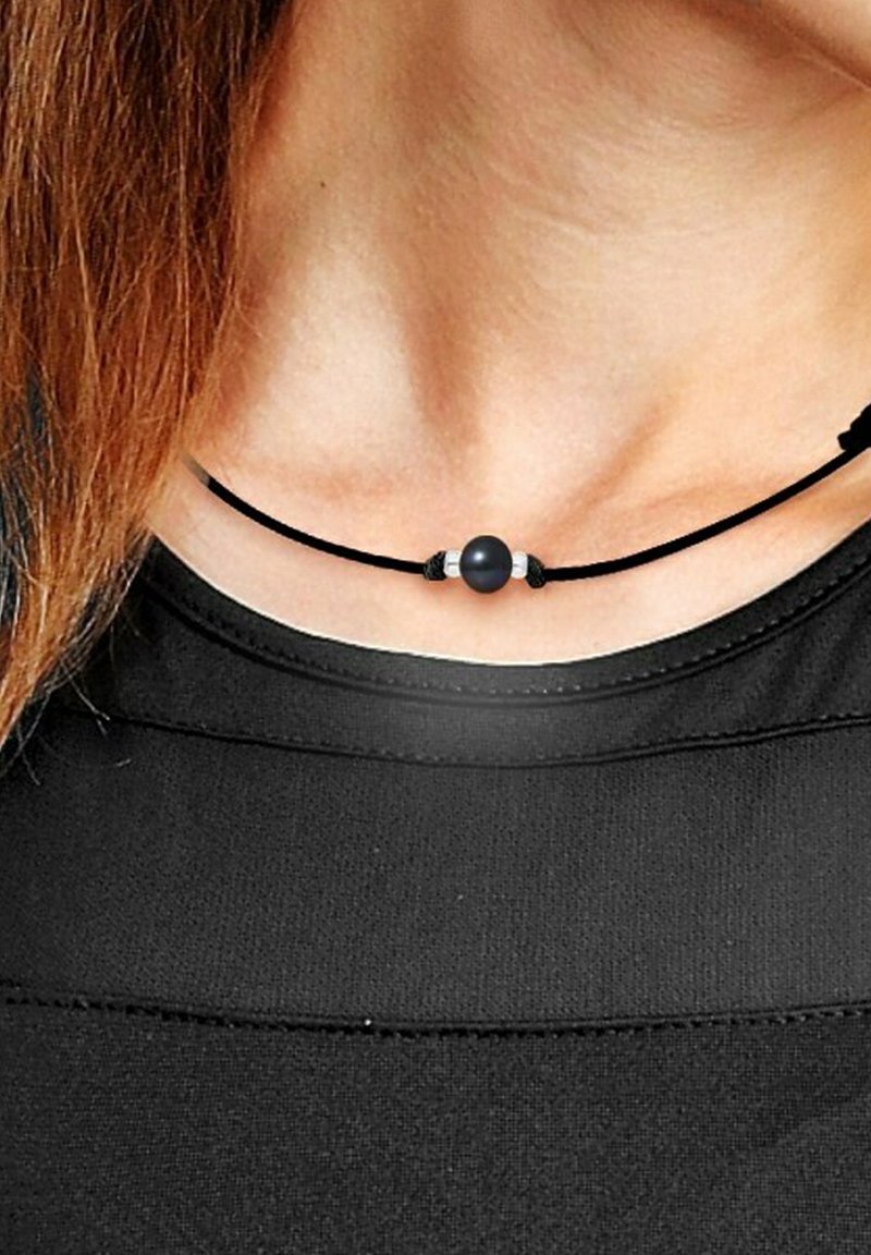Collier en cordon noir avec une perle noire centrale, accentuée par des détails en argent de chaque côté, porté sur une chemise noire.