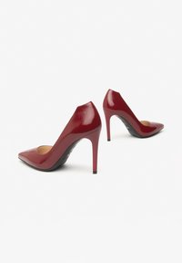Rode lakleren pumps met een spitse neus, slanke stilettogoed, en een gladde afwerking. Heeft een uitsnede aan de achterkant en een zwarte zool.