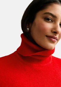 Czerwony sweter typu golf z prążkowanym wzorem, o wysokim dekolcie, fakturowanej tkaninie i dopasowanym kroju. Posiada gładkie, miękkie wykończenie i minimalne zdobienia.