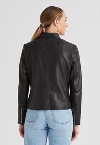 Schwarze Lederjacke mit einer taillierten Passform, ausgestattet mit einem Stehkragen und Reißverschlussärmeln, kombiniert mit hellblauen Jeans.