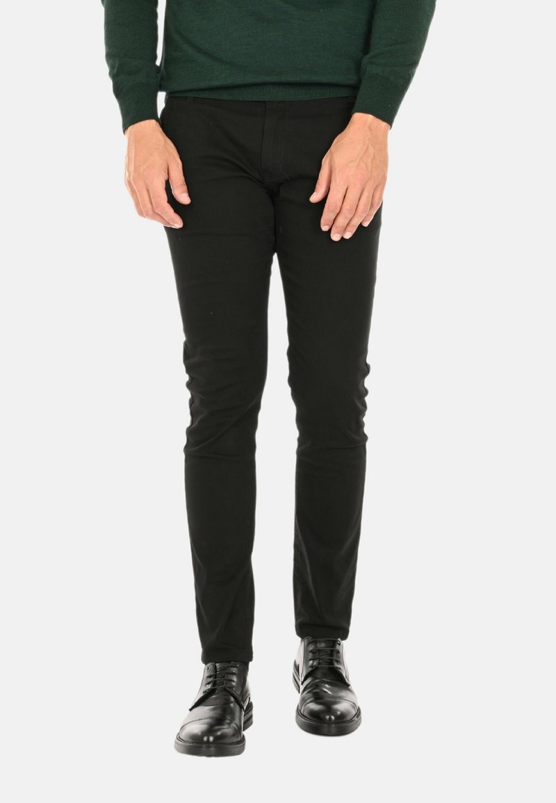 Pantaloni neri aderenti realizzati in tessuto liscio, con un classico design a cinque tasche, abbinati a scarpe nere stringate.