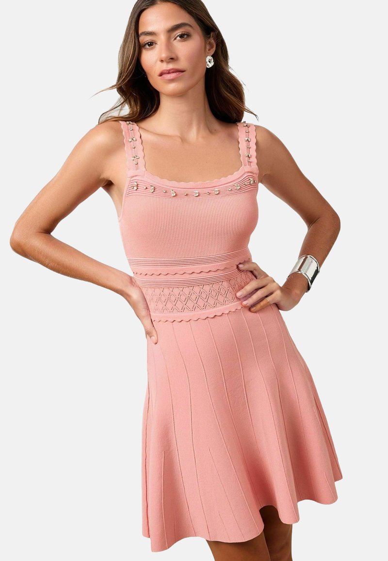 Rochie roz cu dungi, cu margini ondulate, bretele decorative și talie texturată. Fustă evazată cu linii verticale și țesătură netedă.