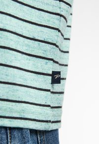 Lichtgroen gestreept T-shirt met donkergrijze horizontale lijnen; zachte textuur; voorzien van een klein blauw label met een logo aan de zoom.