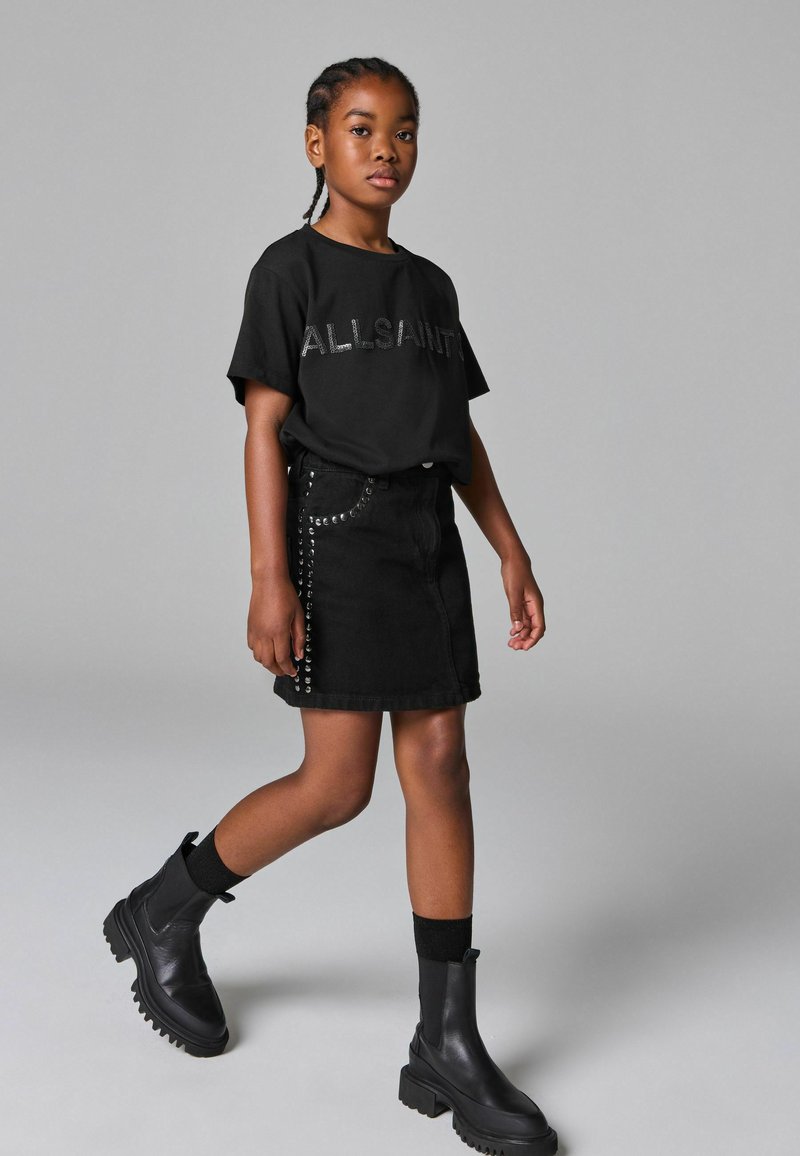 Svart t-shirt med kort ärm med "ALLSAINTS" logotyp, ihopparad med en svart denimkjol med nitar, och svarta ankelstövlar.