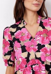 Květinové šaty s černým pozadím, na kterém jsou velké růžové a béžové květiny, poloviční rukávy, výstřih do V a sukně v patrovém designu.