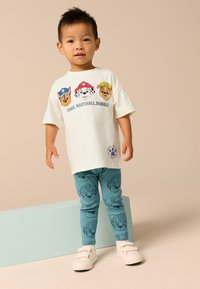 White cotton t-shirt featuring three cartoon dog characters, paired with blue leggings with printed dog faces, and white shoes.