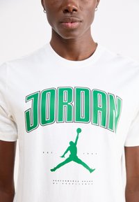 Hvid bomulds T-shirt med fedt grønt "JORDAN" tekst og en sort silhuet af en basketballspiller, med "EST. 1984" nedenfor.