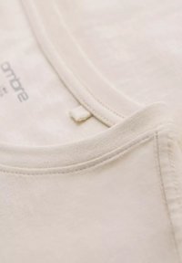 Lys beige bomulds t-shirt med rund hals, blød tekstur og minimale syninger. Inkluderer et lille mærke nær kraven.